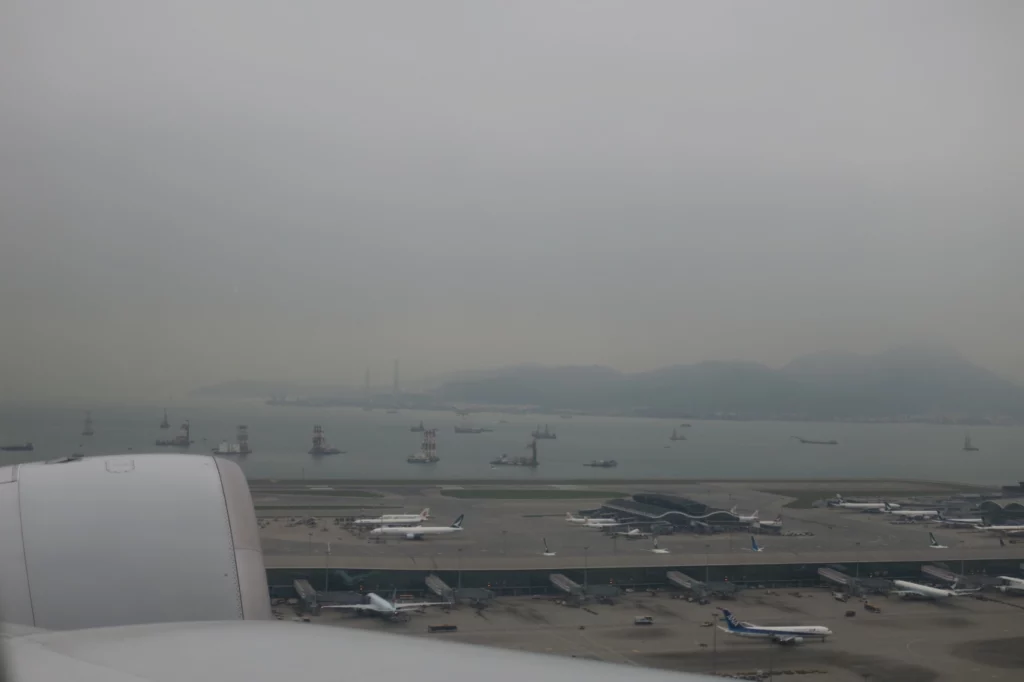 an airplane wing on a runway with many airplanes and a body of water