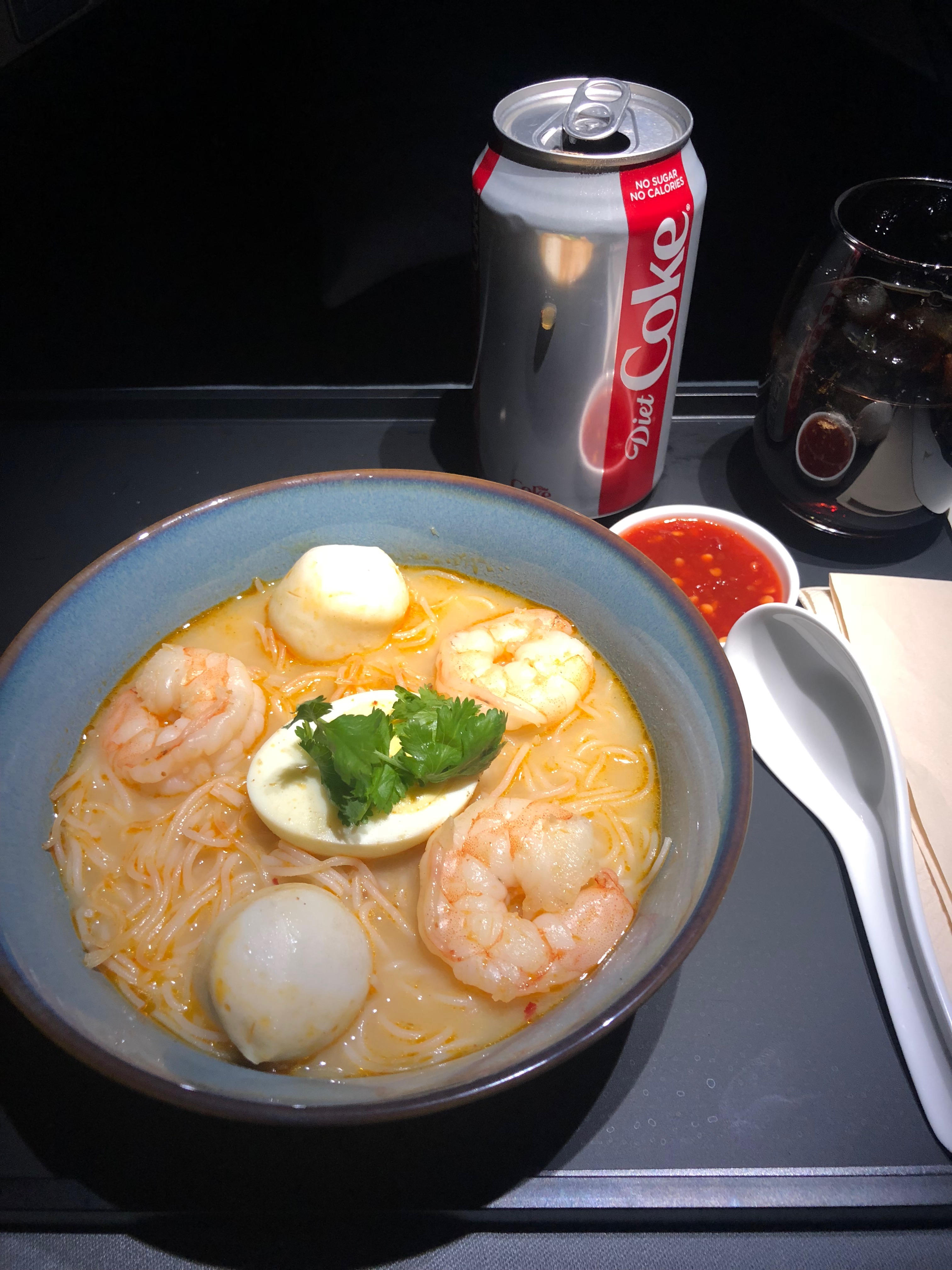 a bowl of soup with shrimp and noodles and a can of soda