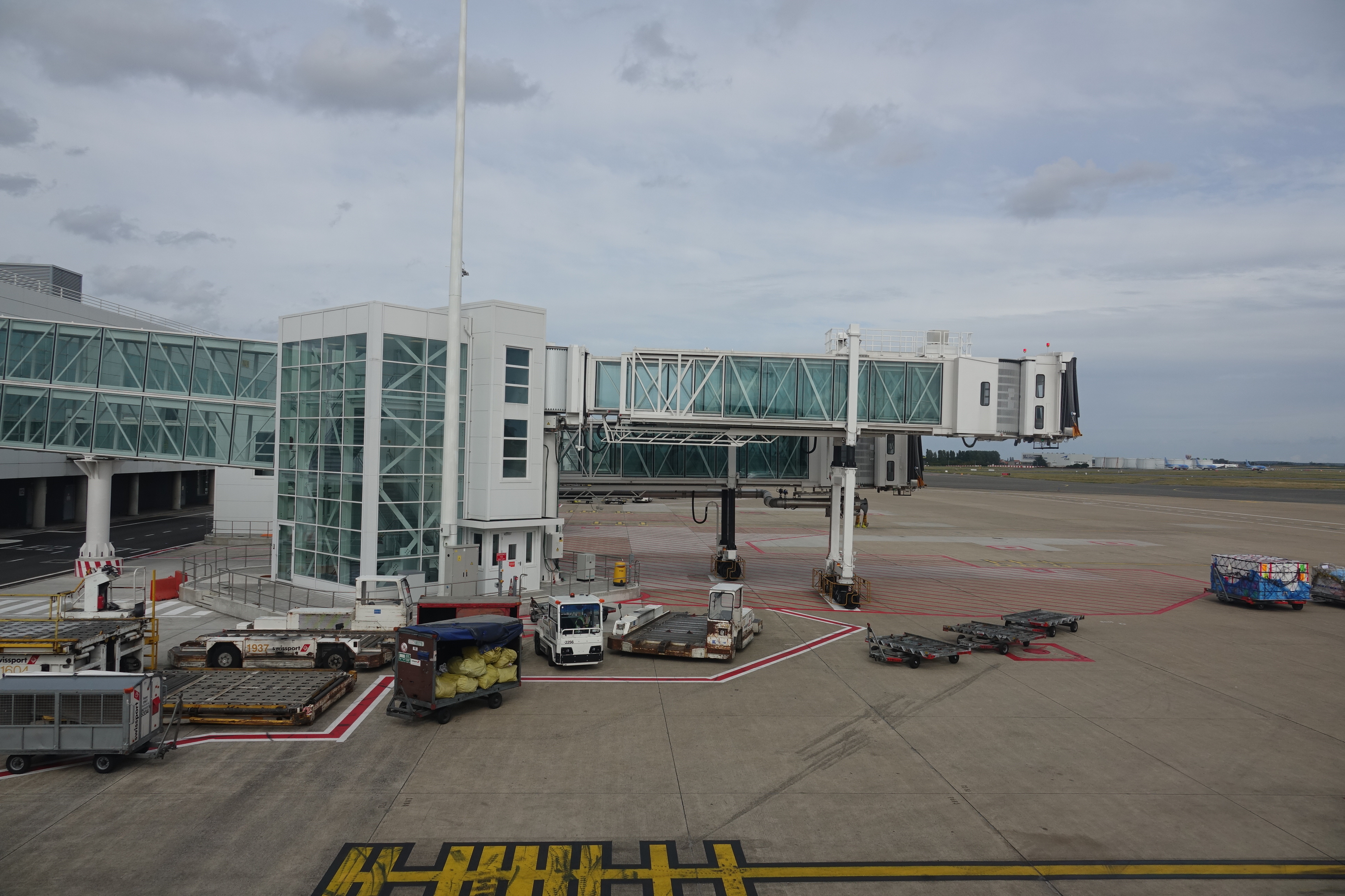 a white building with a bridge and luggage carts on a runway