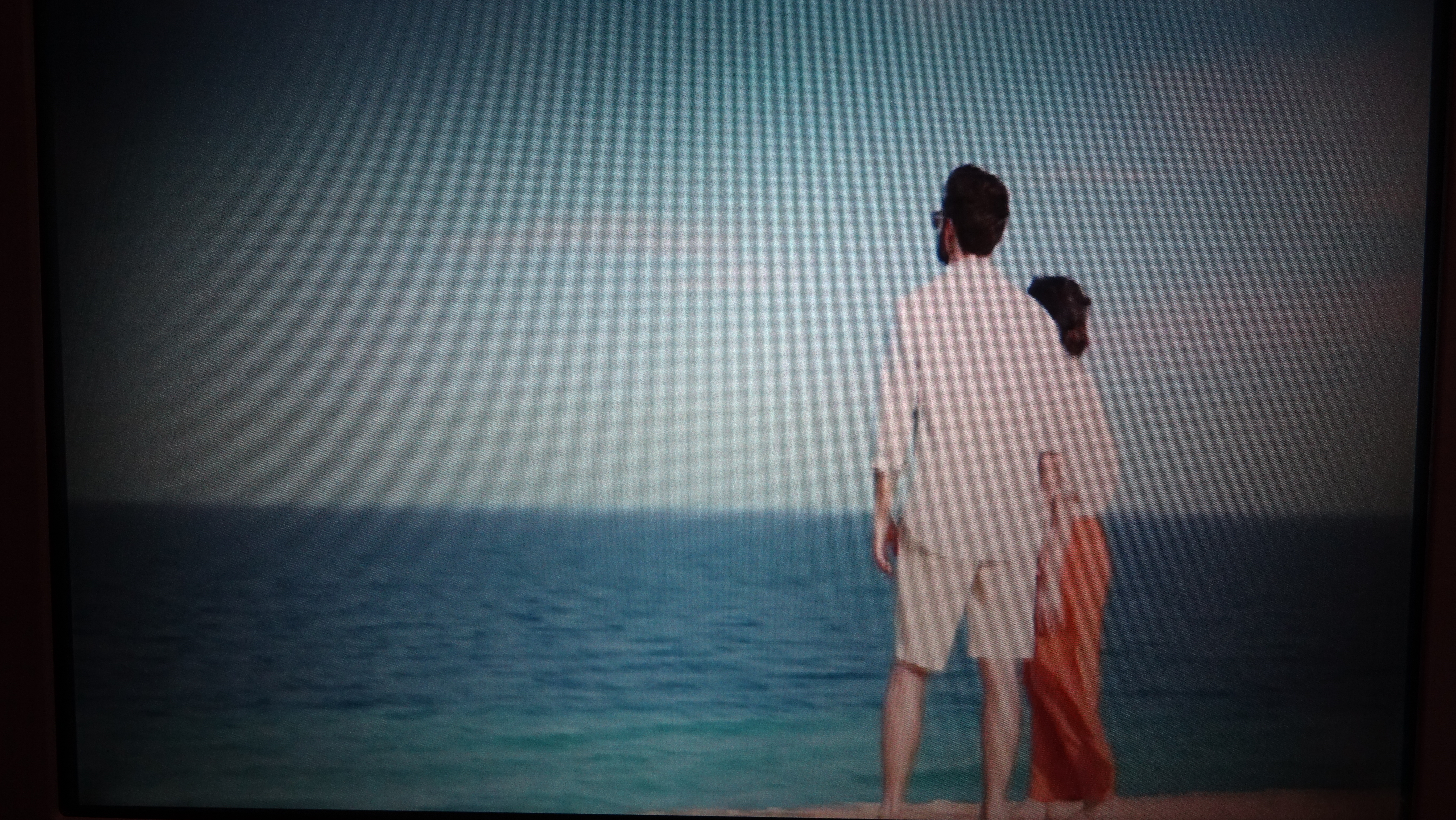 a man and woman standing on a beach looking at the ocean