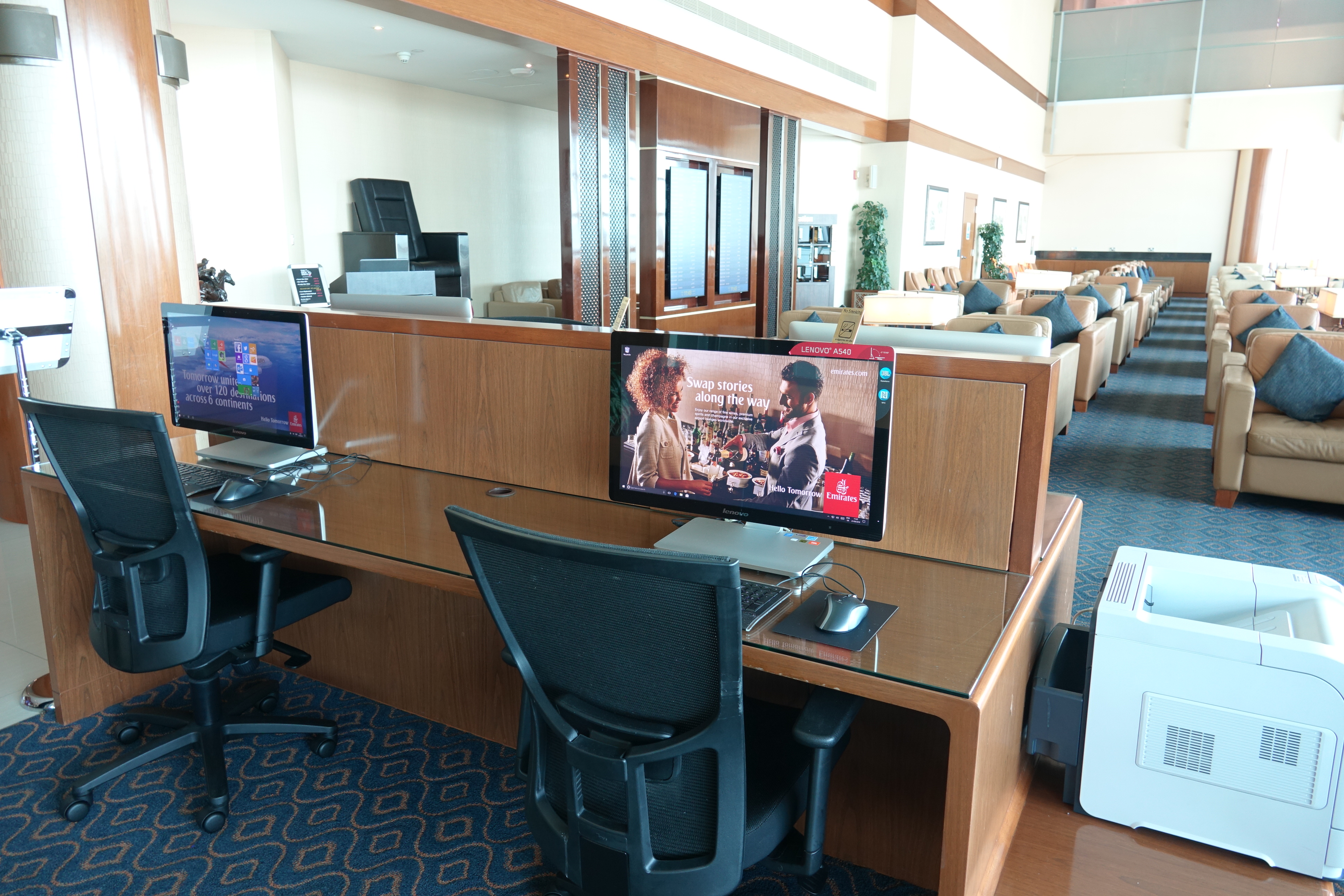 a desk with computers and chairs in a room with a large window