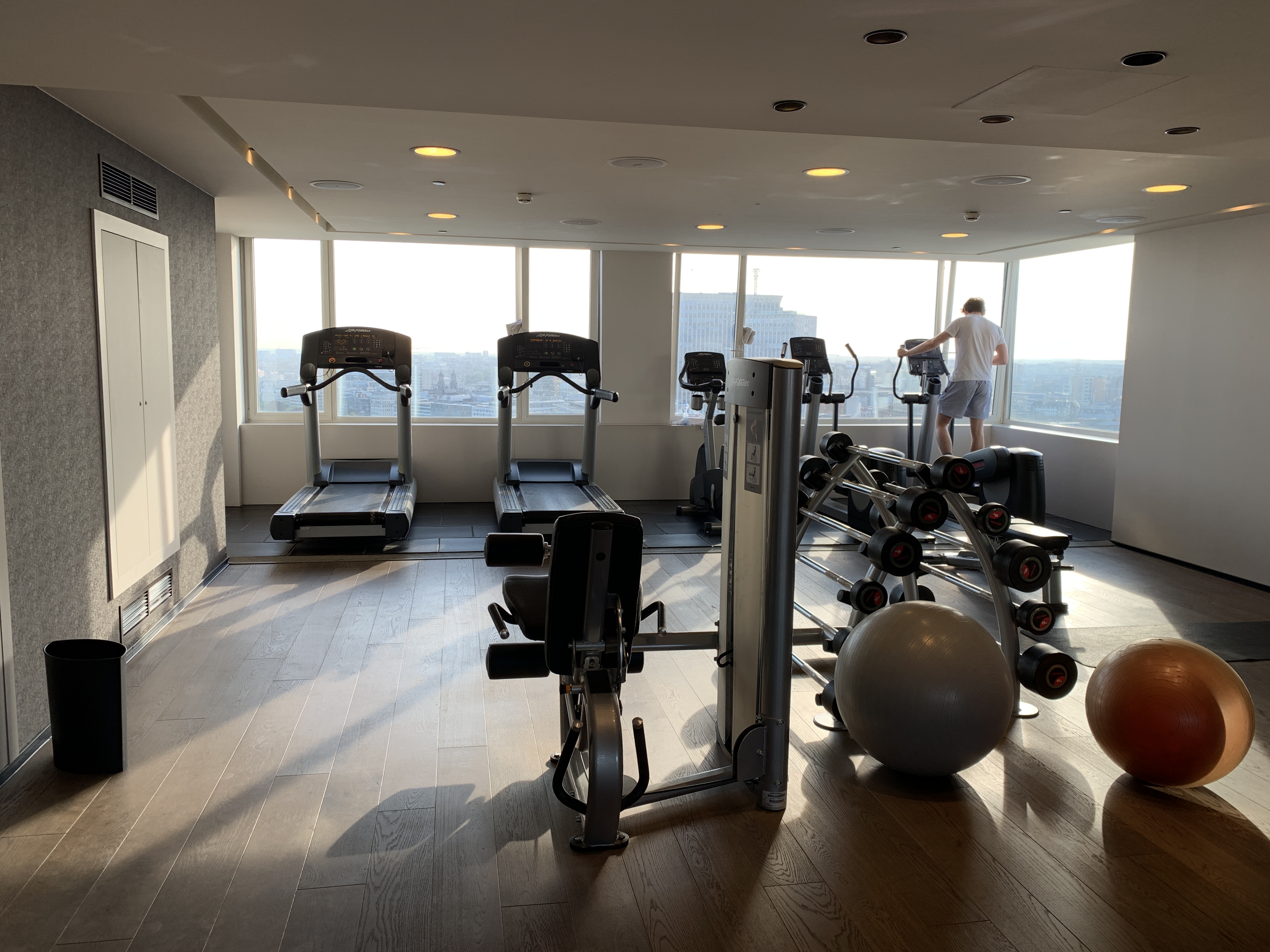 a gym with exercise equipment and a man standing in front of a window