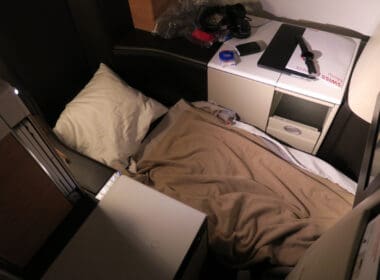 a bed with a blanket and a laptop on a desk