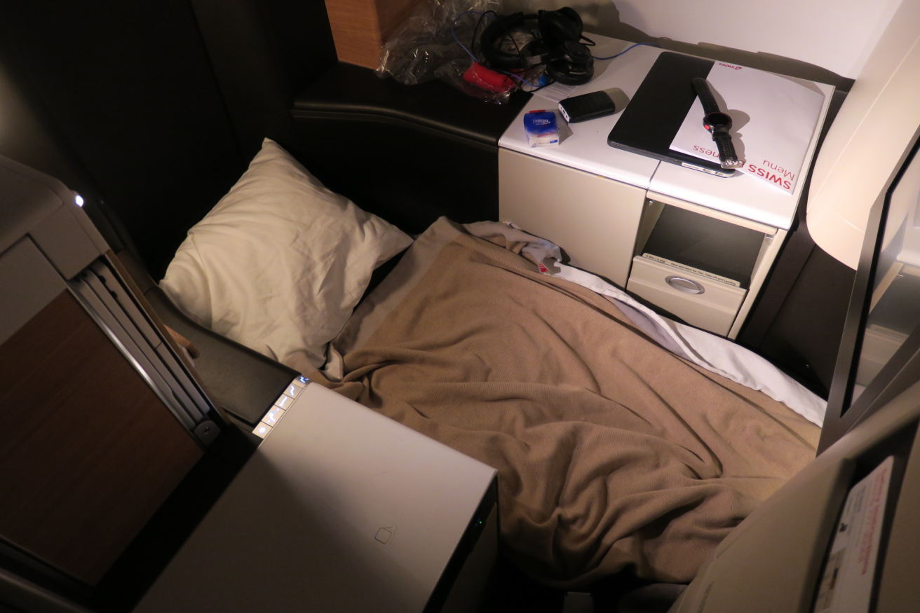 a bed with a blanket and a laptop on a desk