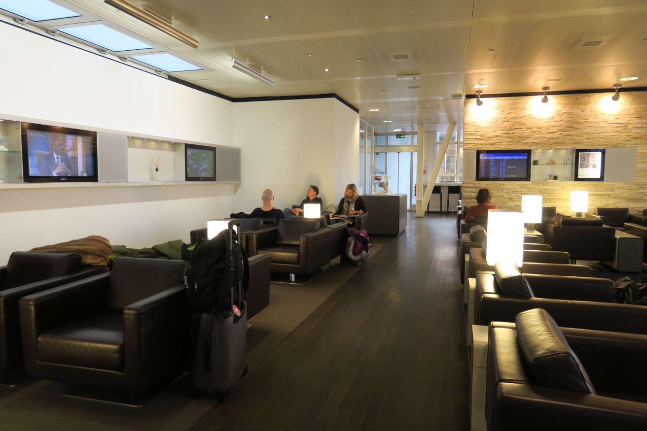 people sitting in a room with black chairs and a television on the wall