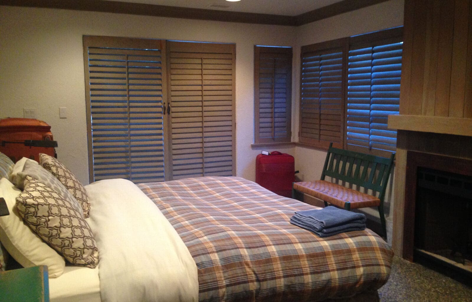 a bed with a blanket and a bench in a room with shutters