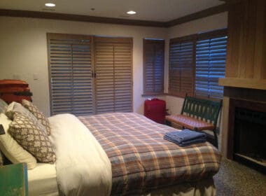 a bed with a blanket and a bench in a room with shutters