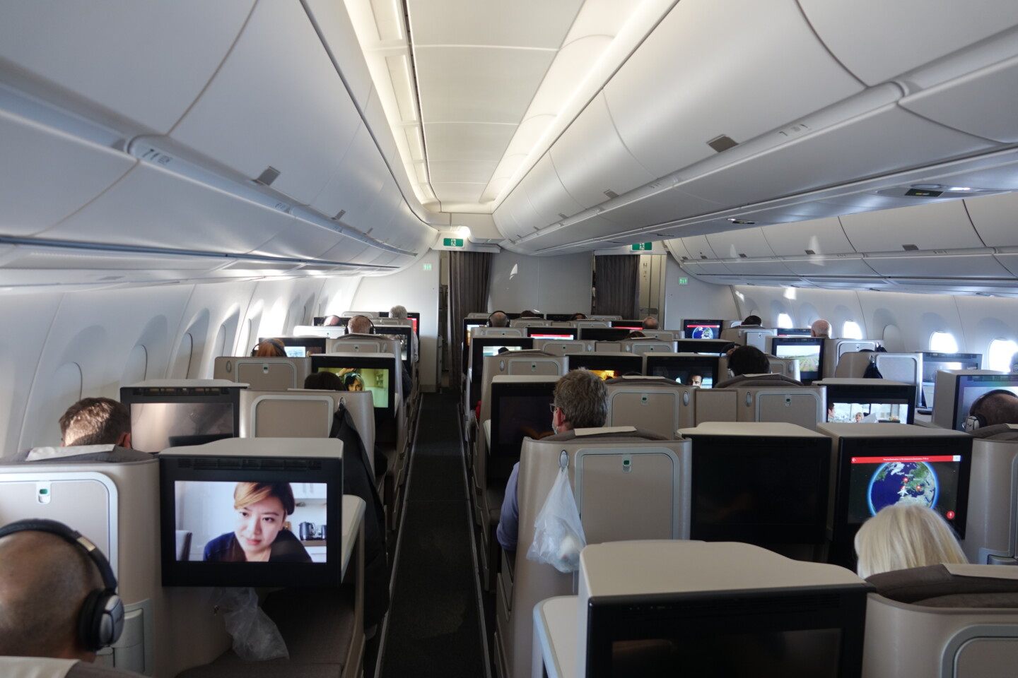 a group of people sitting in an airplane with monitors on the seats