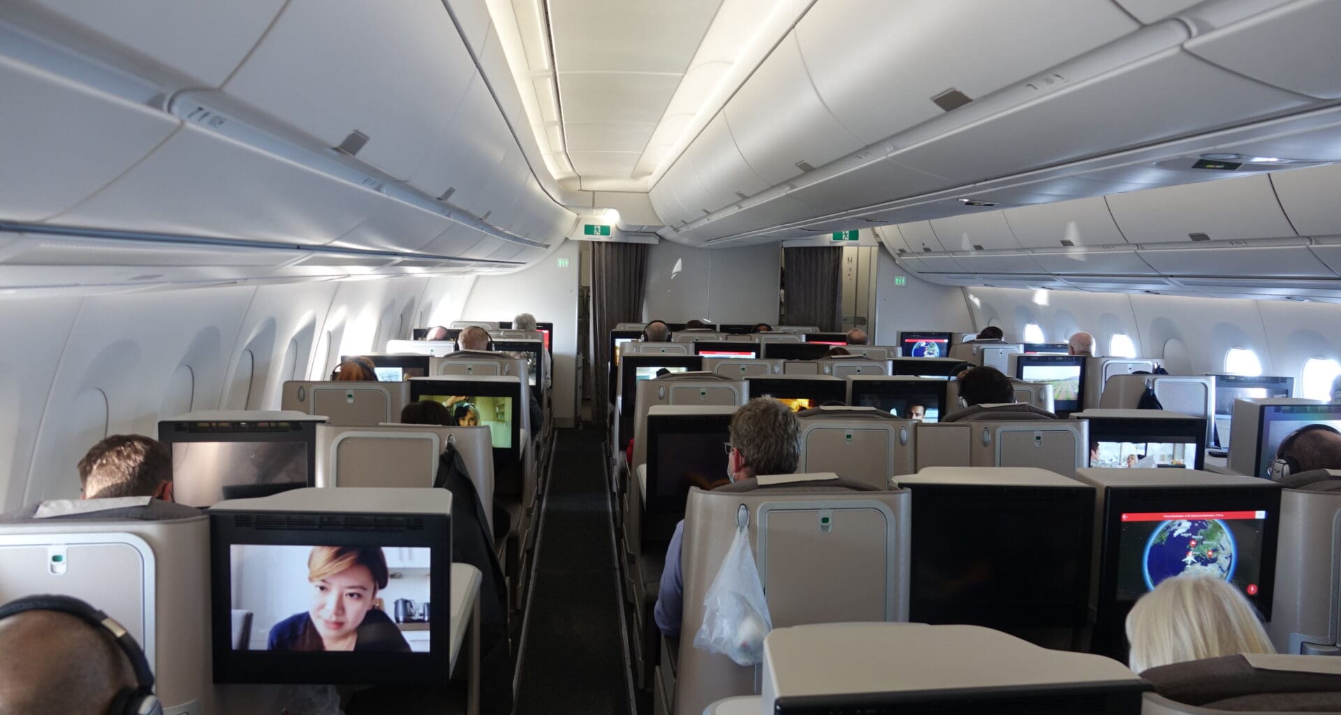 a group of people sitting in an airplane with monitors on the seats