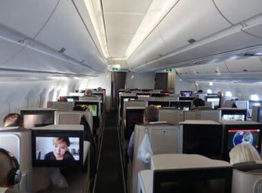 a group of people sitting in an airplane with monitors on the seats