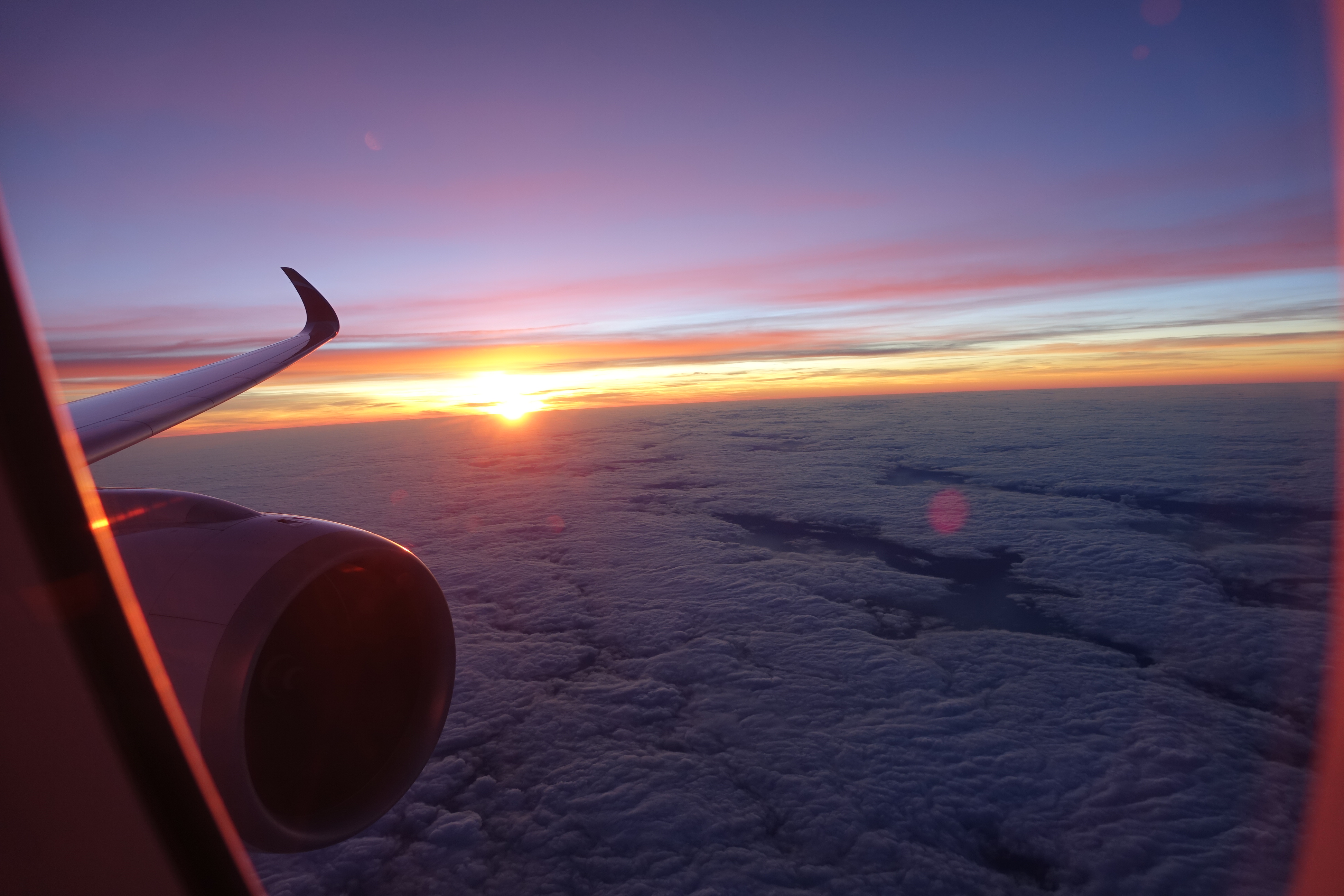 an airplane wing and the sun above clouds