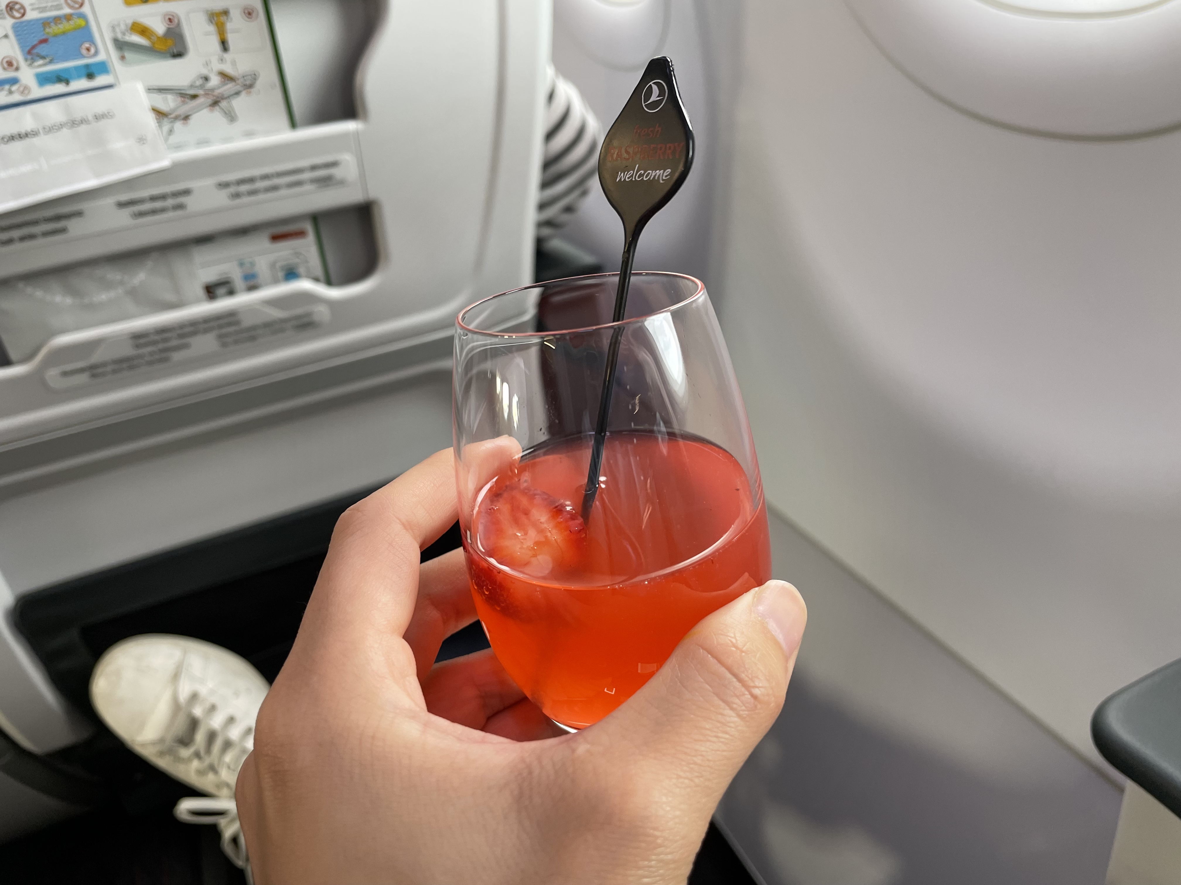 a hand holding a glass of red liquid with a spoon in it