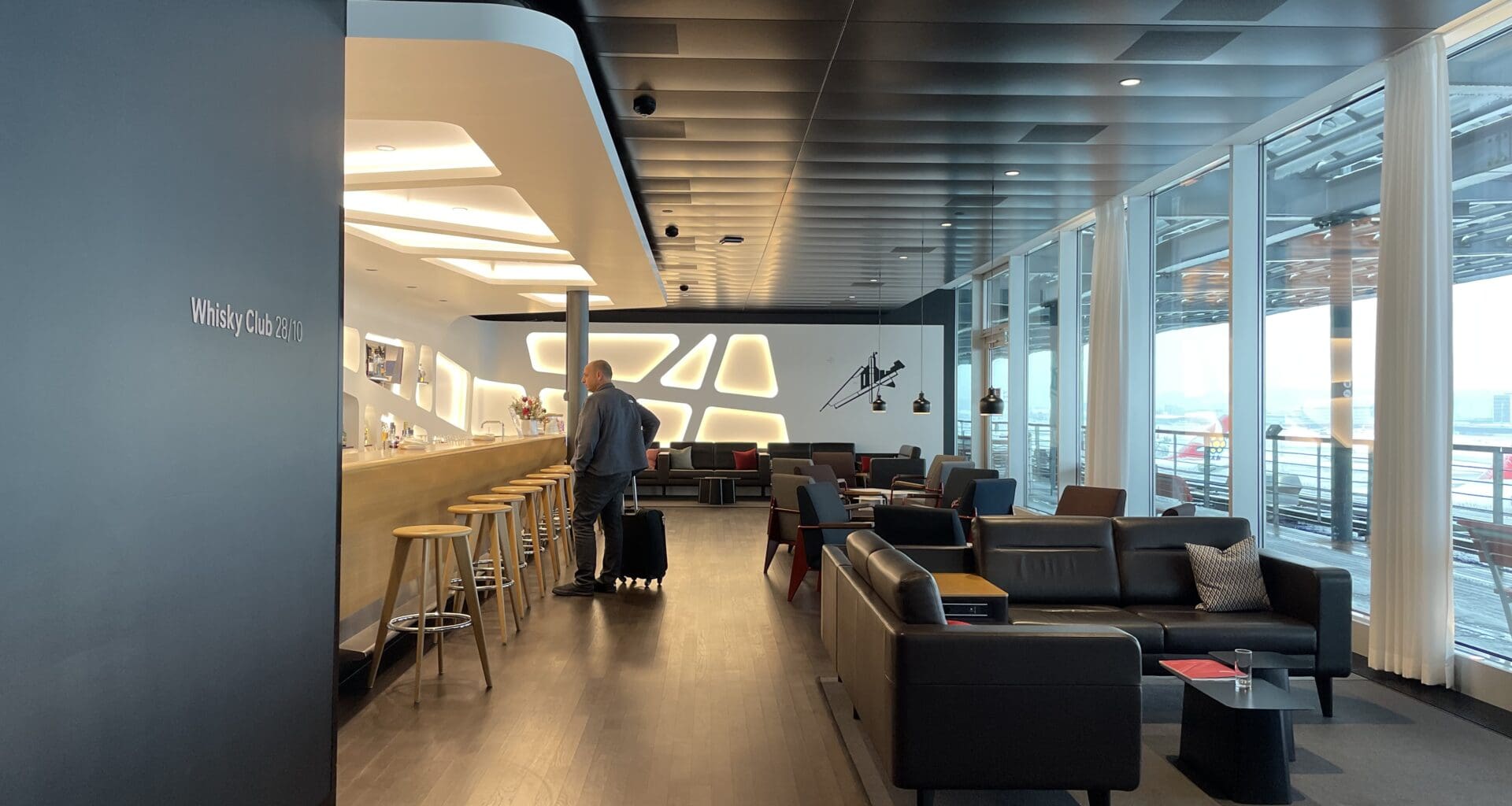 a man with luggage in a room with a bar and chairs