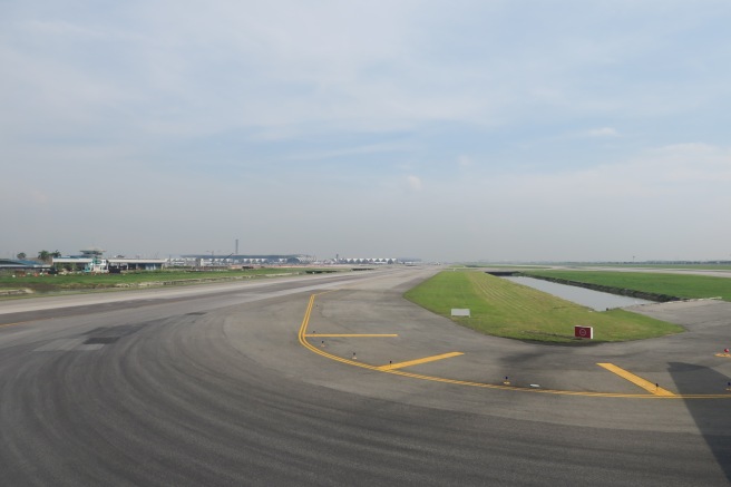 a runway with grass and buildings in the background