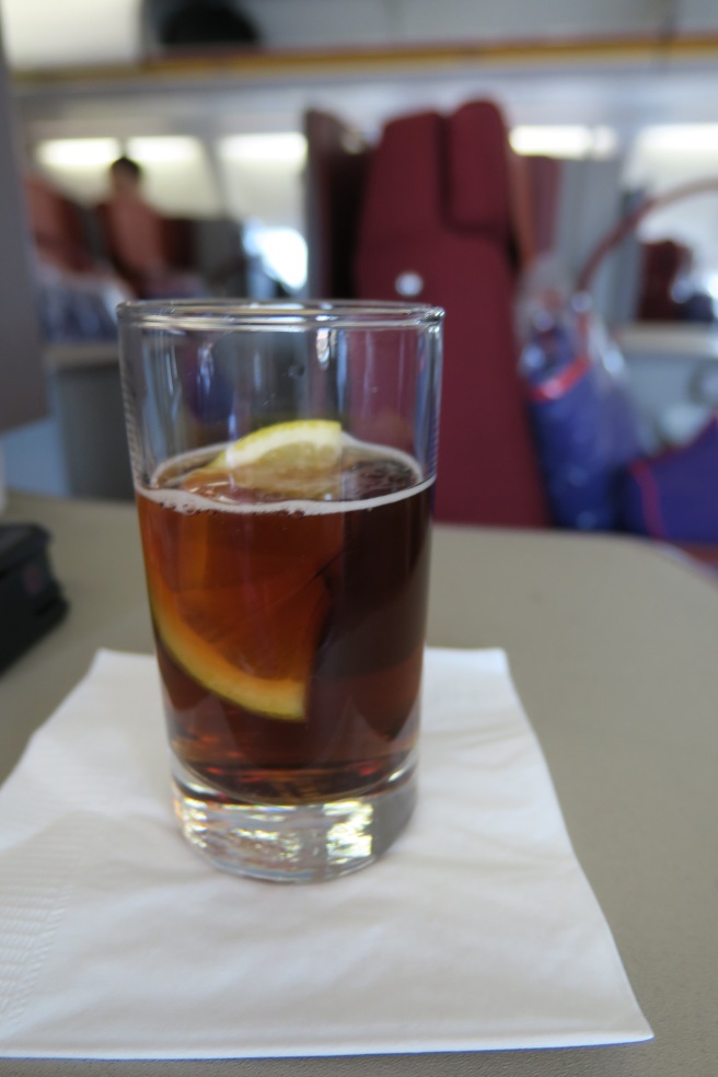 a glass of brown liquid with a lemon slice on a napkin