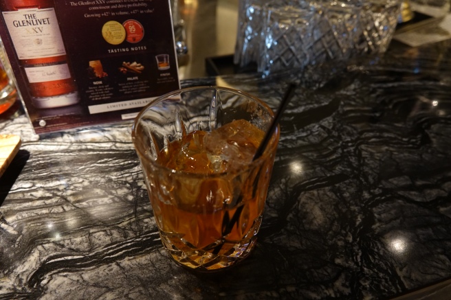 a glass of amber liquid with ice and a straw on a table