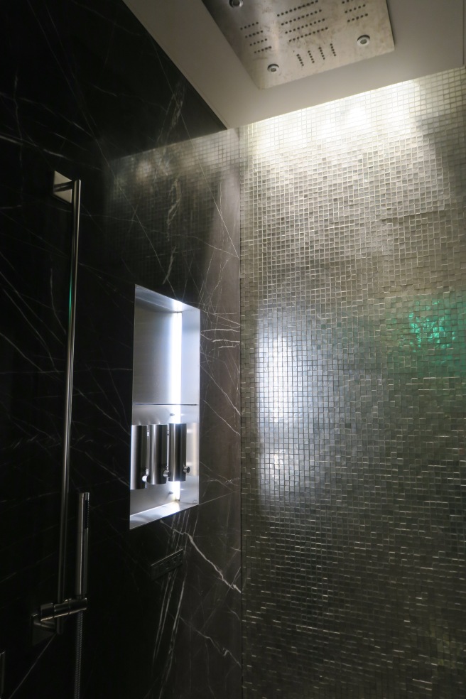 a bathroom with a tile wall and a silver shelf