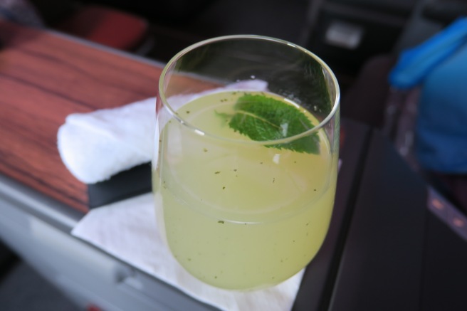 a glass of yellow liquid with a leaf on top of it