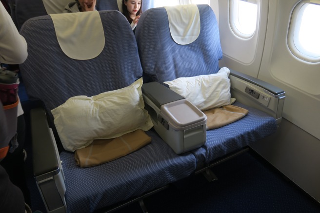 a seat on an airplane with a cooler and pillows