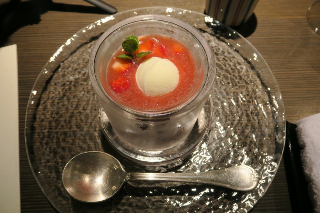 a glass of red liquid with ice cream and mint on a plate