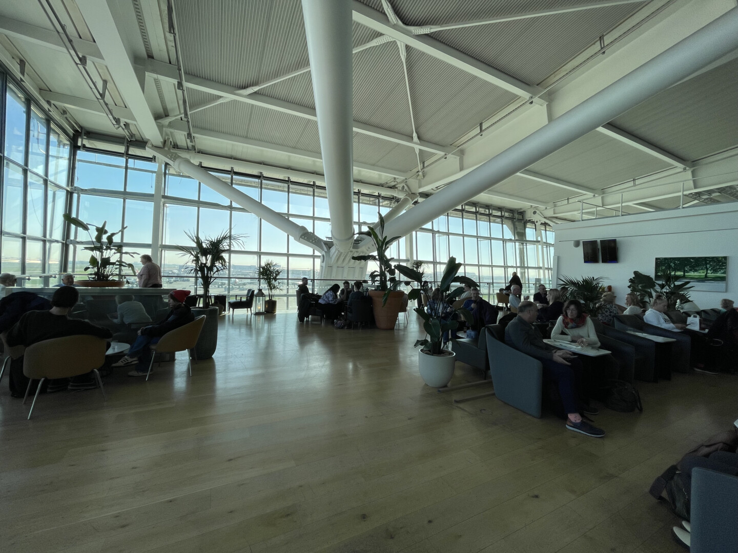 a large room with many people sitting and plants