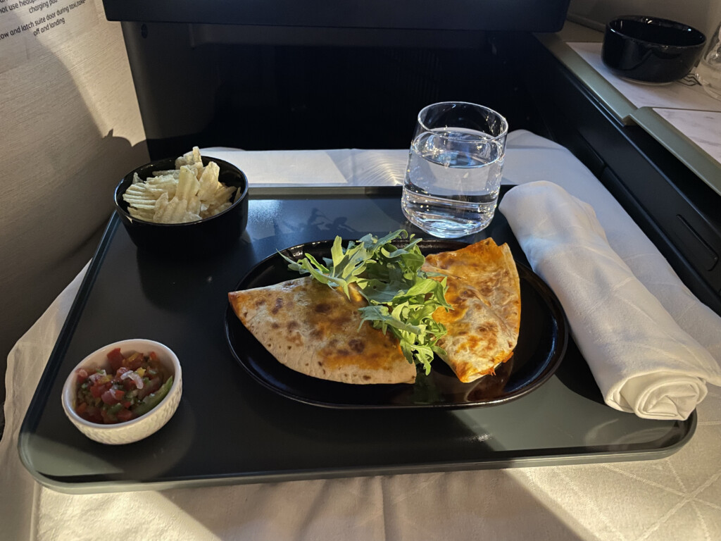 food on a tray with a glass of water and a bowl of chips