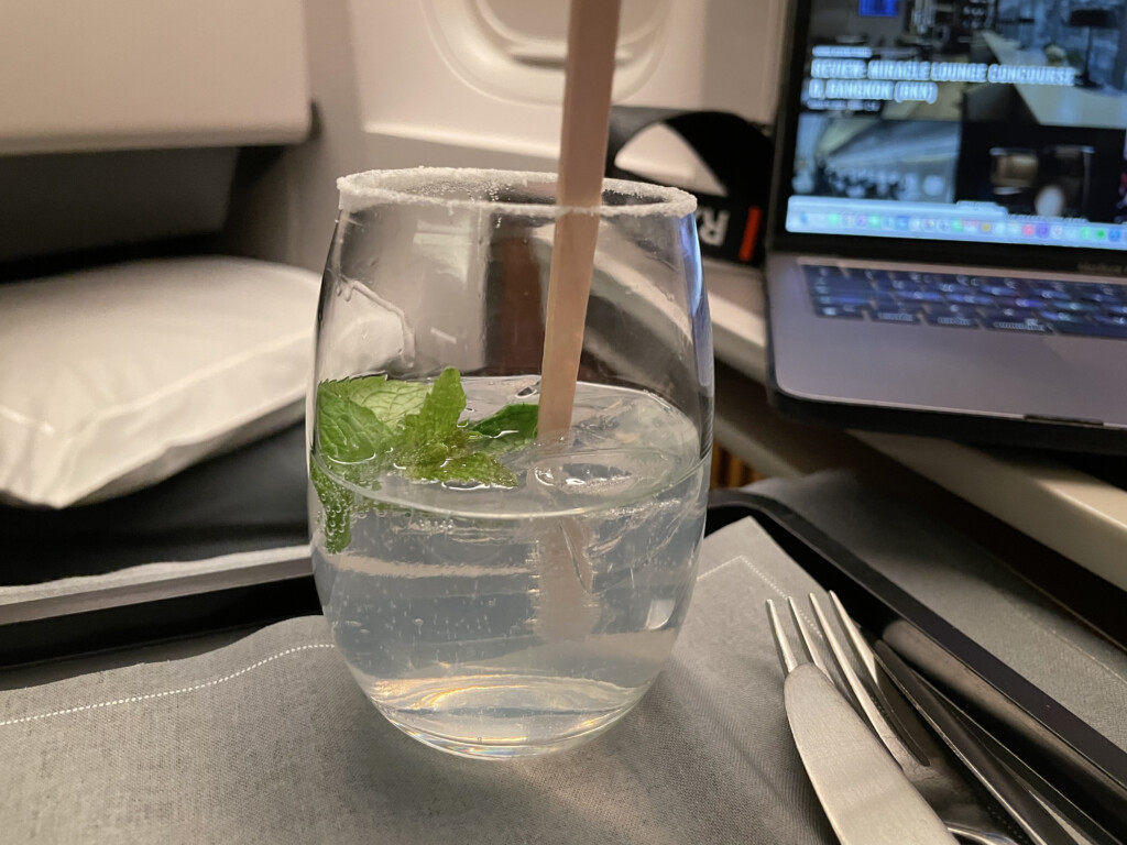 a glass with liquid and a wooden straw in front of a laptop