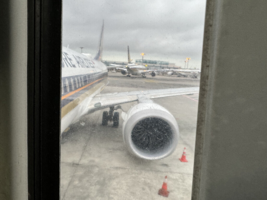 a window with a plane engine and other airplanes on the ground