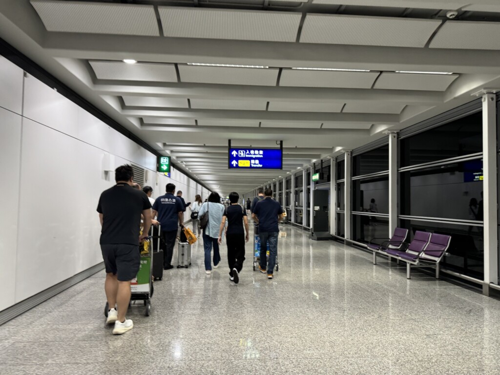 people walking in a hallway with chairs and a sign