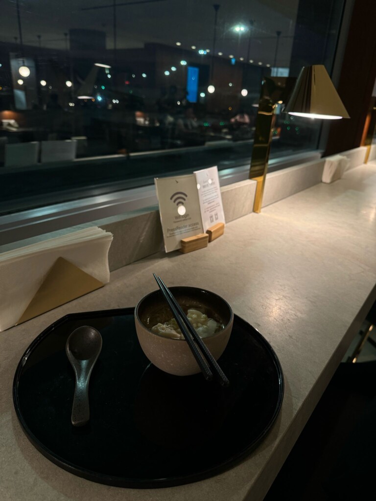 a bowl of soup with chopsticks on a black plate and a spoon on a black plate