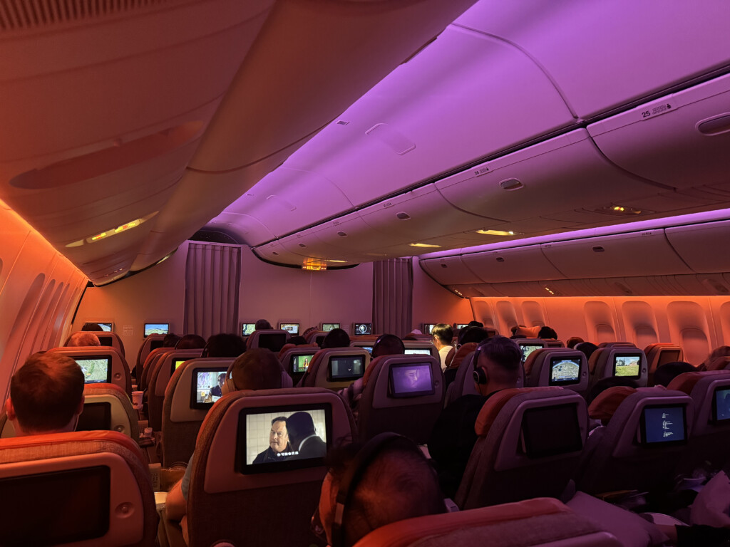a group of people sitting in an airplane with monitors on the seats