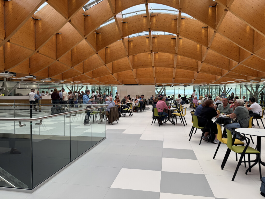 a group of people sitting at tables in a room with a glass roof