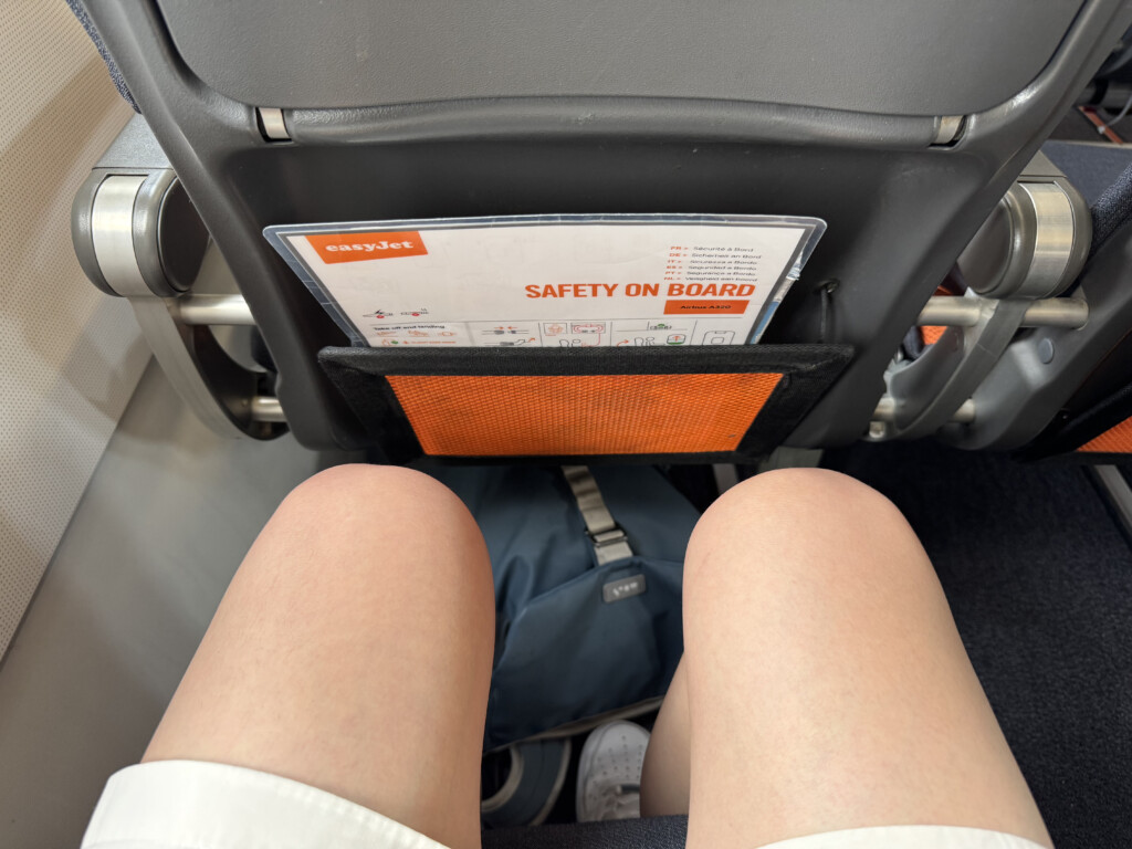 a person's legs in a seat with a safety card in the pocket