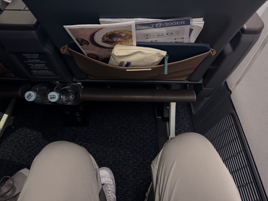 a person's legs and a bag with food and a drink in the back of a seat