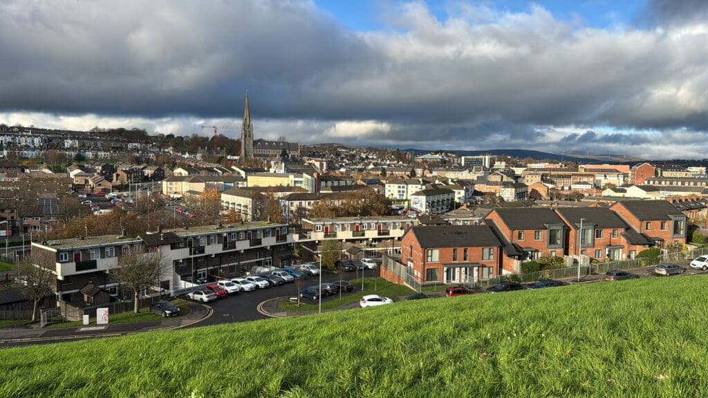 a green hill with cars parked in front of a city