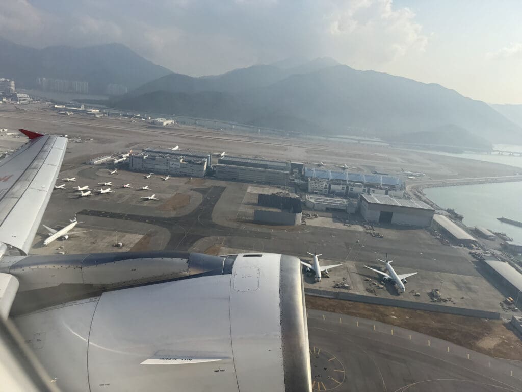 an airplane wing and a runway with buildings and mountains in the background