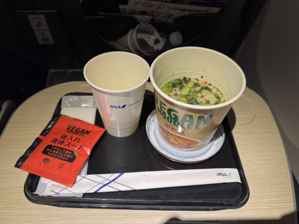 a tray with two cups of soup and a packet of soy sauce